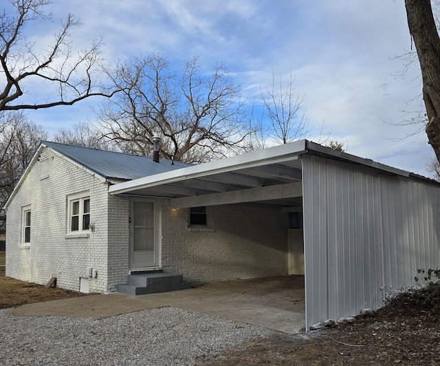 view of property exterior featuring gravel driveway, brick siding, entry steps, metal roof, and an attached carport