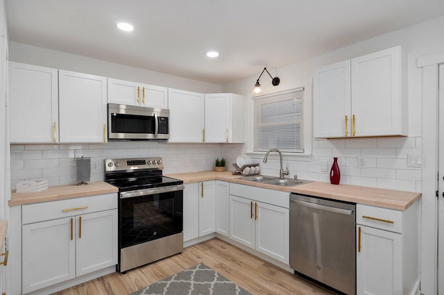 kitchen featuring light wood finished floors, butcher block counters, a sink, stainless steel appliances, and backsplash