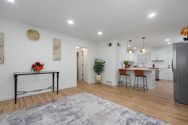 kitchen with light wood-style flooring, appliances with stainless steel finishes, a peninsula, a kitchen bar, and white cabinetry