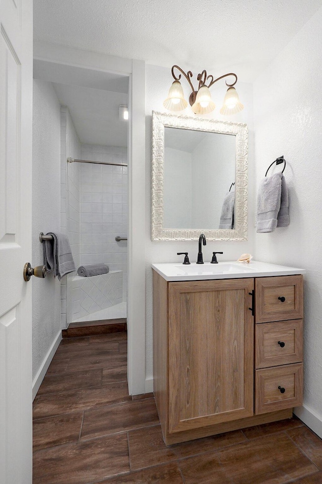 bathroom with baseboards, a tile shower, wood finished floors, and vanity