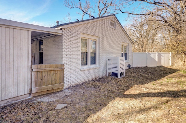 view of property exterior with a gate, brick siding, and fence