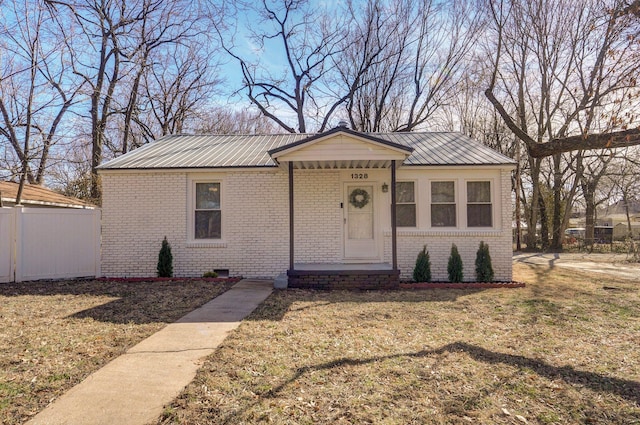 view of front facade with a front yard, fence, metal roof, and brick siding