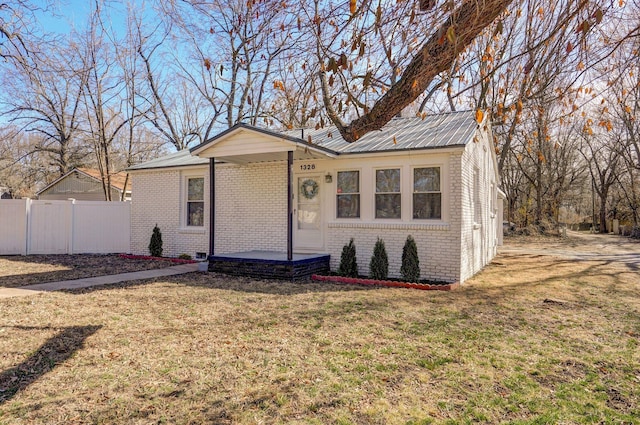 bungalow-style house with metal roof, covered porch, brick siding, fence, and a front yard