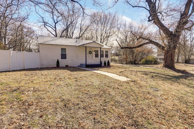 rear view of property with brick siding, a lawn, crawl space, fence, and metal roof