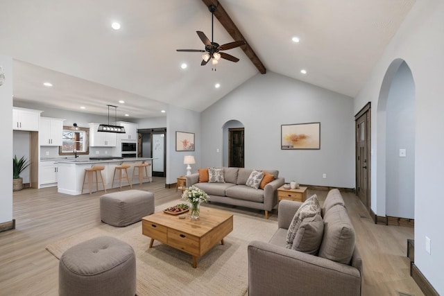 living room with arched walkways, beam ceiling, light wood-style flooring, high vaulted ceiling, and baseboards