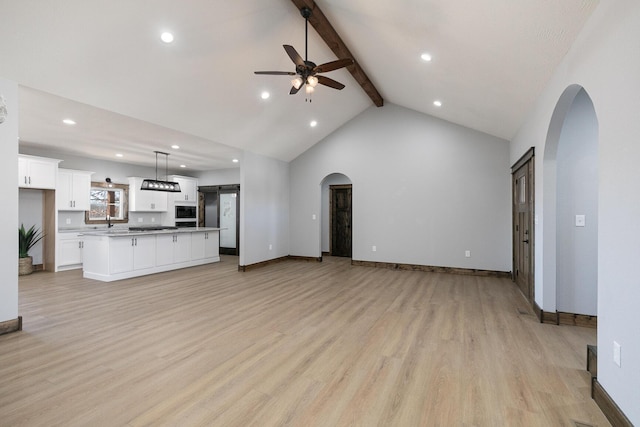 unfurnished living room featuring arched walkways, light wood-style floors, a ceiling fan, beamed ceiling, and baseboards