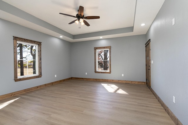 empty room featuring baseboards, light wood-style flooring, ceiling fan, a tray ceiling, and recessed lighting