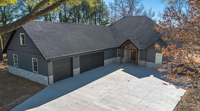 view of front of home featuring a garage, stone siding, roof with shingles, and concrete driveway