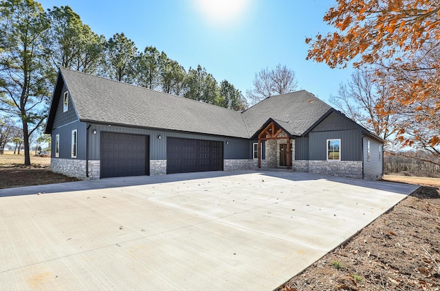 view of front of home featuring an attached garage, stone siding, driveway, and roof with shingles