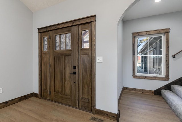 entrance foyer featuring visible vents, arched walkways, baseboards, light wood-style flooring, and stairway