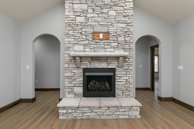 unfurnished living room featuring a fireplace, arched walkways, vaulted ceiling, and wood finished floors