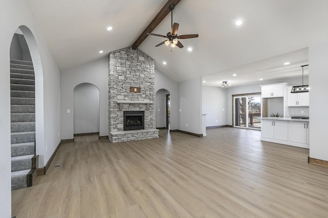 unfurnished living room with light wood-type flooring, a stone fireplace, stairway, and beam ceiling