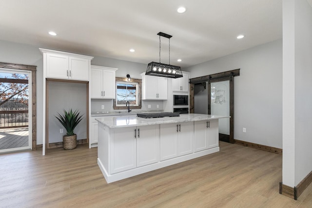 kitchen featuring black microwave, a barn door, a sink, white cabinets, and a center island