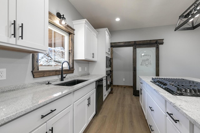 kitchen with a barn door, wood finished floors, a sink, white cabinets, and black appliances