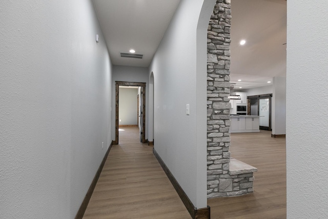 corridor featuring light wood-style flooring, a barn door, visible vents, and baseboards