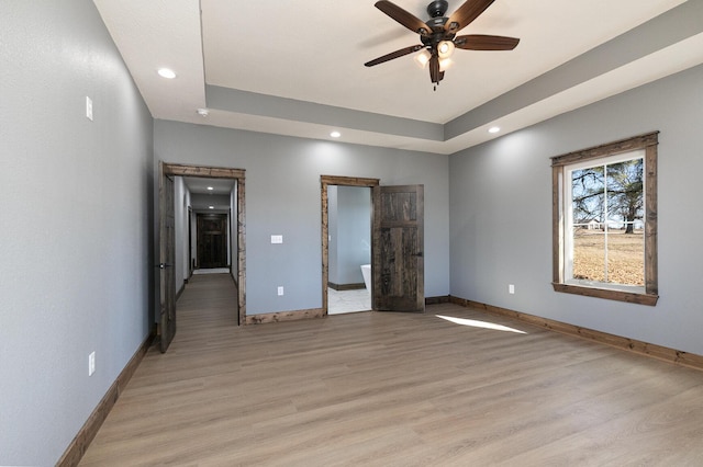 unfurnished bedroom featuring baseboards, a ceiling fan, a tray ceiling, light wood-type flooring, and recessed lighting