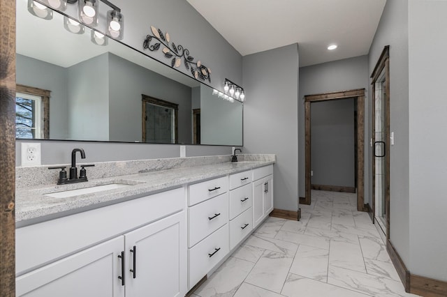 bathroom featuring double vanity, marble finish floor, baseboards, and a sink