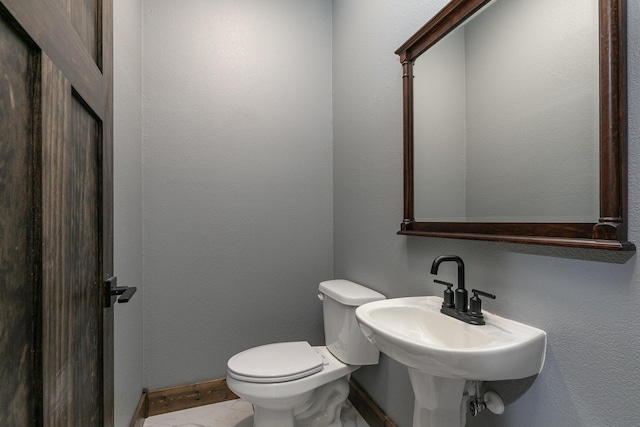 half bathroom with toilet, baseboards, and a sink