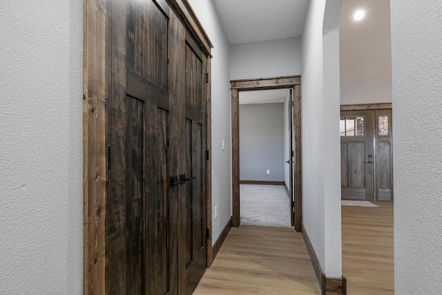 corridor with a textured wall, light wood-style flooring, and baseboards