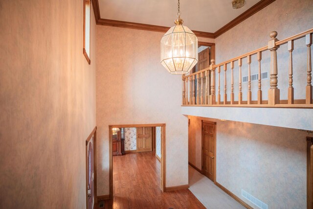 stairway with ornamental molding, visible vents, a notable chandelier, and wood finished floors