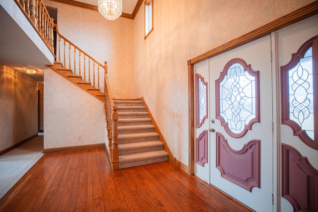 entrance foyer featuring a notable chandelier, wood-type flooring, ornamental molding, baseboards, and stairs