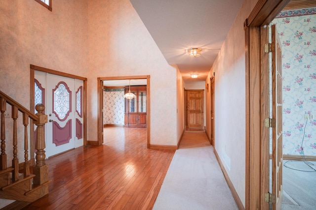 foyer entrance featuring hardwood / wood-style flooring, a towering ceiling, stairway, baseboards, and wallpapered walls