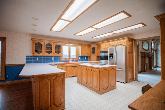 kitchen featuring wallpapered walls, a wainscoted wall, appliances with stainless steel finishes, light countertops, and a sink