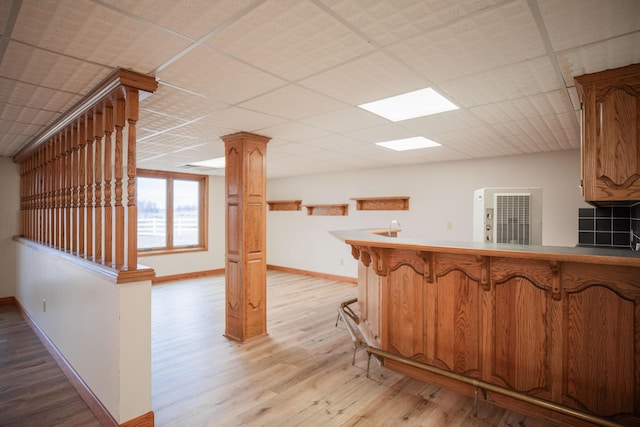 kitchen featuring a paneled ceiling, baseboards, light wood-style flooring, a peninsula, and a kitchen bar