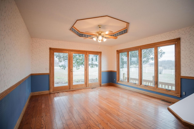 empty room featuring ceiling fan, a wainscoted wall, visible vents, hardwood / wood-style floors, and wallpapered walls