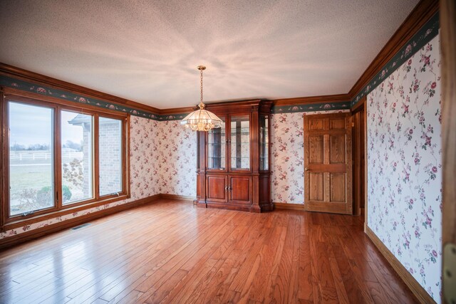 unfurnished dining area with wallpapered walls, baseboards, hardwood / wood-style floors, an inviting chandelier, and a textured ceiling