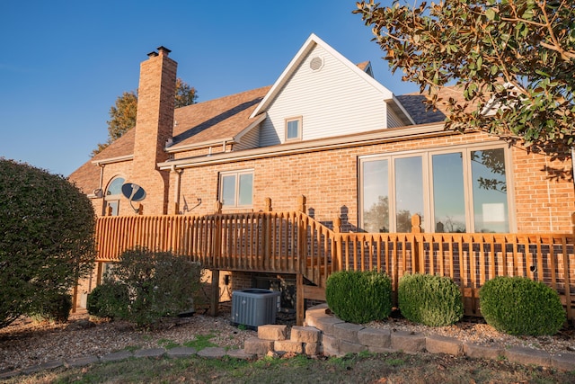 back of property with a shingled roof, a chimney, central AC unit, and brick siding