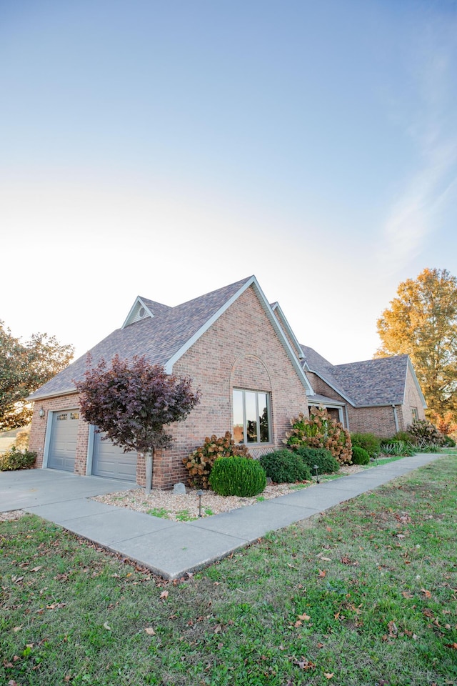 view of property exterior featuring brick siding, a shingled roof, concrete driveway, a lawn, and an attached garage