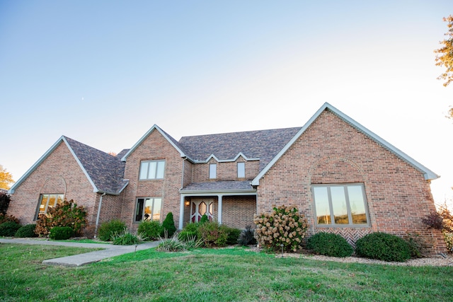 traditional home with a shingled roof, a front lawn, and brick siding