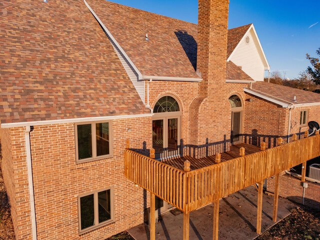 back of property featuring a shingled roof, brick siding, a chimney, and a deck