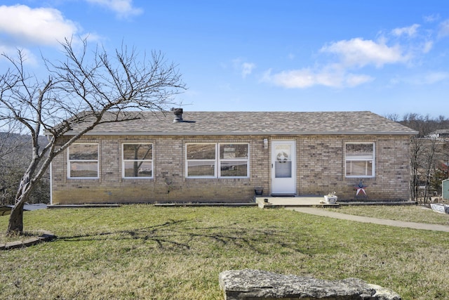 view of front of home featuring a shingled roof, a front yard, and brick siding