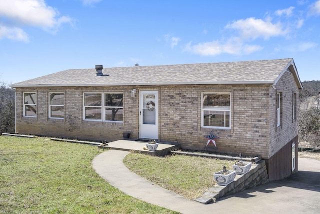 view of front facade with a shingled roof, a front lawn, and brick siding