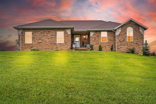 view of front of home with brick siding, a shingled roof, and a yard