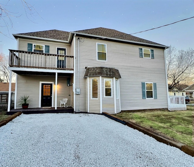 back of house with a yard, a shingled roof, and a balcony