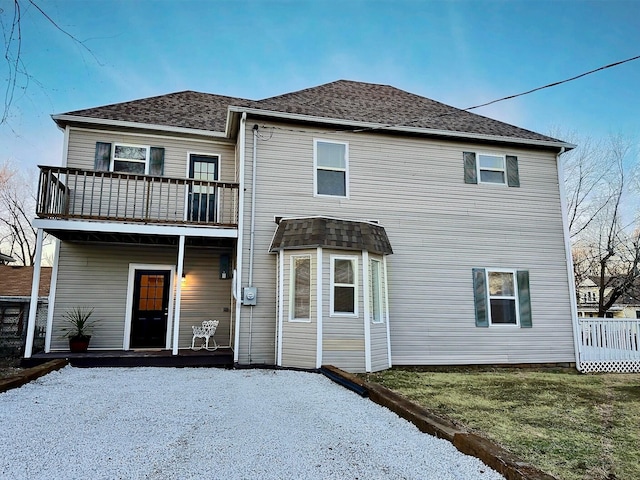 rear view of property with a shingled roof, a yard, and a balcony