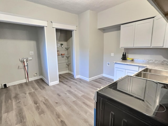 kitchen with light wood finished floors, baseboards, light countertops, a textured ceiling, and white cabinetry