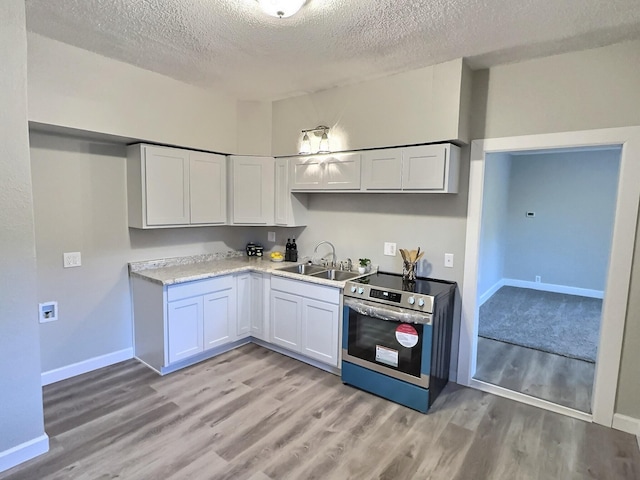 kitchen with electric stove, light countertops, white cabinetry, a sink, and light wood-type flooring