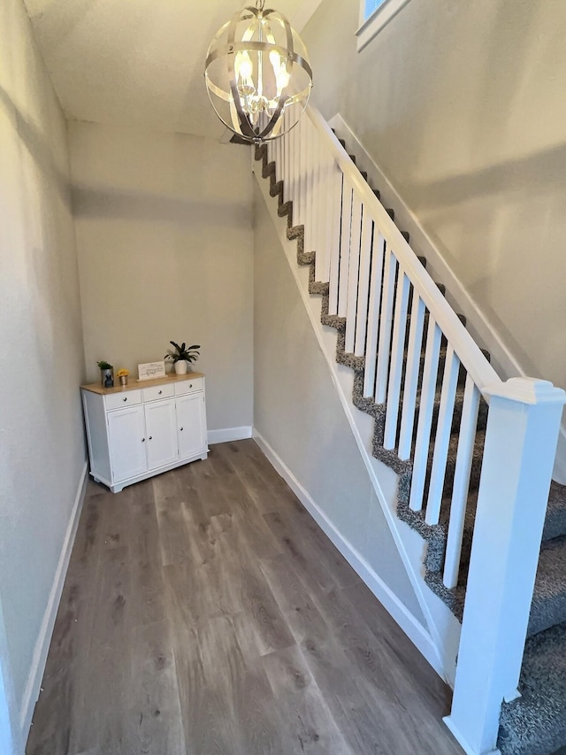 staircase featuring a notable chandelier, baseboards, and wood finished floors