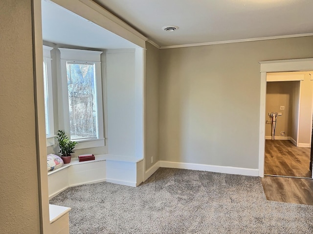 carpeted spare room with baseboards, visible vents, wood finished floors, and ornamental molding