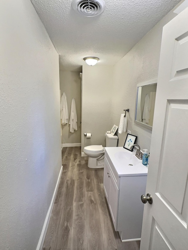 bathroom featuring a textured ceiling, toilet, wood finished floors, vanity, and visible vents