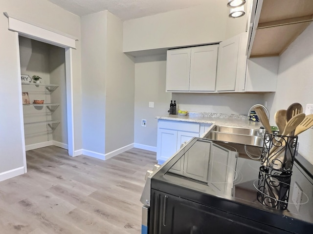 kitchen featuring a sink, white cabinets, baseboards, light countertops, and light wood finished floors