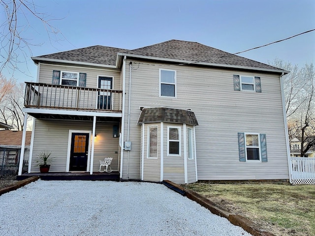 back of house featuring a balcony and a shingled roof