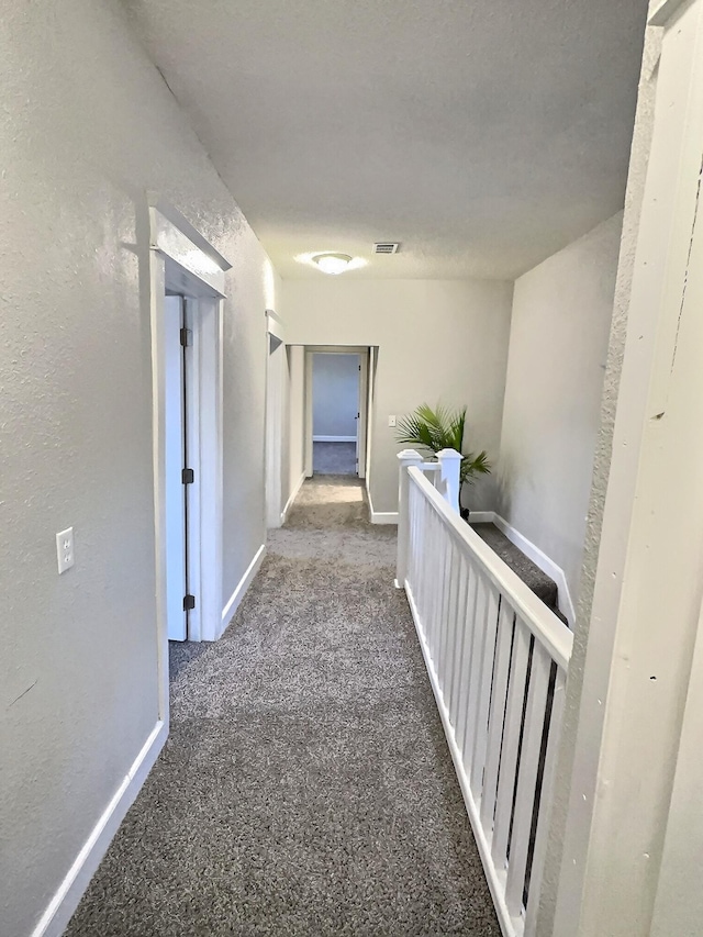 corridor featuring carpet floors, visible vents, a textured wall, and baseboards