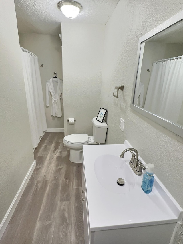 full bath with baseboards, toilet, wood finished floors, a textured ceiling, and vanity