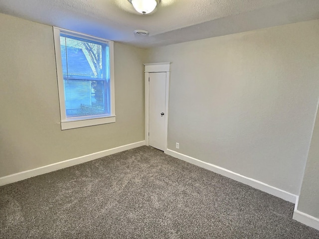 unfurnished room with a textured ceiling, dark carpet, visible vents, and baseboards