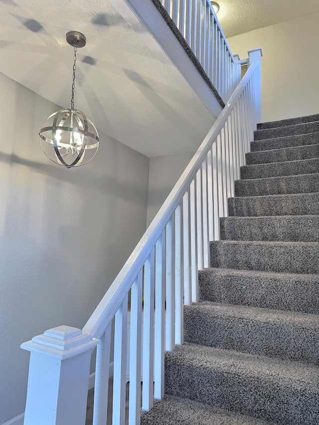 staircase with a notable chandelier and a textured ceiling